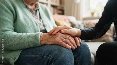 Obraz na płótnie A close-up shot of a younger person gently holding the hands of an elderly woman, symbolizing care, comfort, compassion, and support