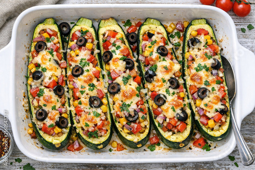 A rectangular baking dish brimming with oven-baked stuffed zucchinis, generously topped with tomatoes and olives. A delicious vegetable entree or side dish.