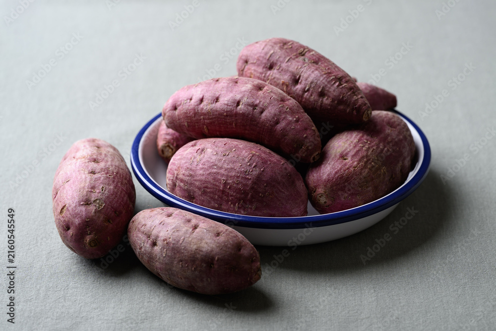 Fototapeta premium Raw purple sweet potatoes in a bowl on cotton fabric background