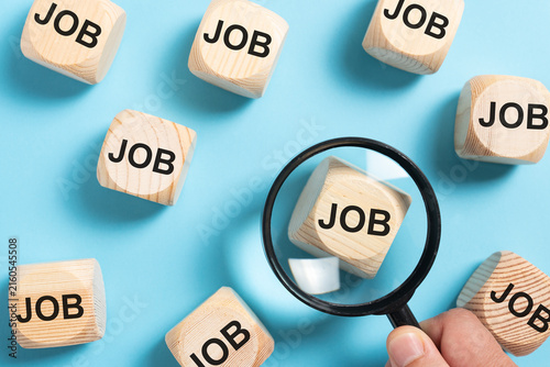 Wooden blocks labeled job arranged on a blue background with a magnifying glass representing employment, recruitment, career searches, hiring, and finding work.