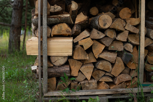 stack of firewood, ustic stack of firewood in a wooden woodshed surrounded by forest greenery, representing home heating, winter preparation, rural living and natural renewable fuel.


