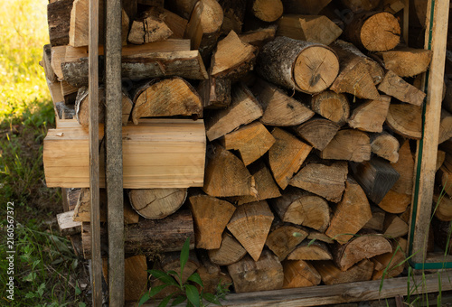 stack of firewood, ustic stack of firewood in a wooden woodshed surrounded by forest greenery, representing home heating, winter preparation, rural living and natural renewable fuel.

