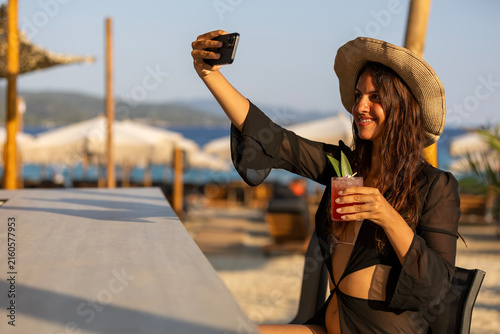 Woman making selfie holding cocktail enjoying beach vacation