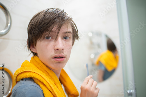 a portrait of a surprised 13-year-old teenage boy with messy hair looking back inside a domestic bathroom at home, experiencing privacy intrusion during morning routine.