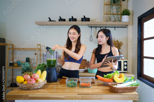 Two asian female friends in sportswear and fruit in home for breakfast drink, healthy diet and green smoothie. Person in kitchen to prepare ingredients, meal prep or nutrition shake for weigh loss
