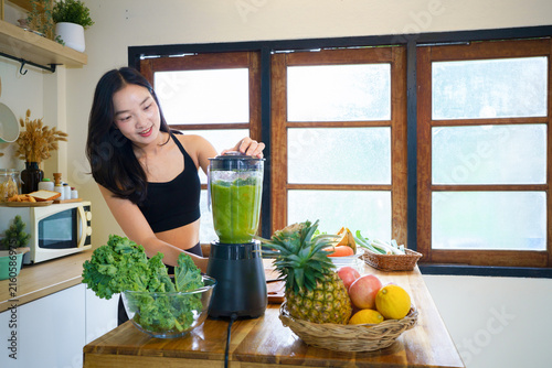 Sporty young woman making healthy green smoothie with blender in the kitchen at home. Healthy lifestyle and dieting concept.
