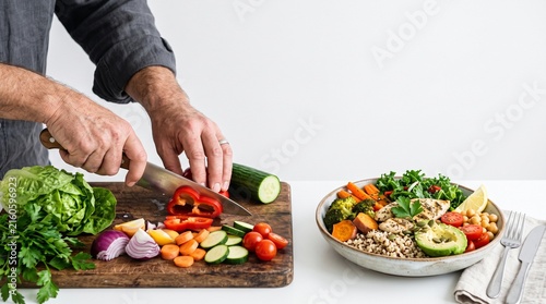 Man preparing a healthy buddha bowl with fresh vegetables and grilled chicken breast