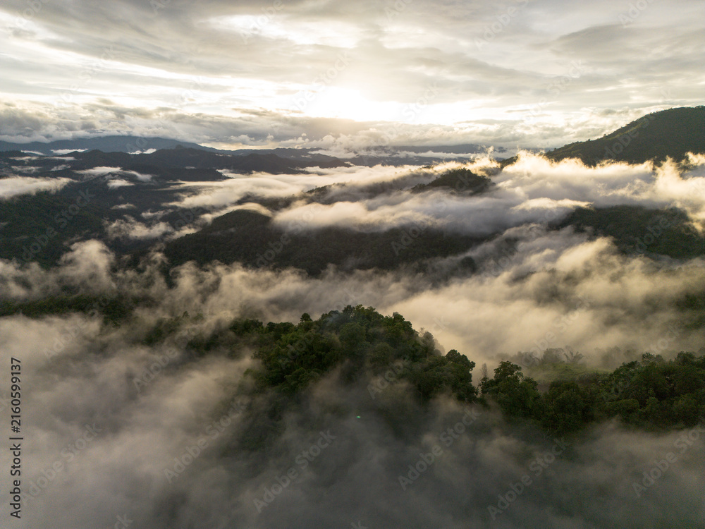 Fototapeta premium Aerial mountain landscape, cloud, forest, mist, and sunrise create dramatic natural panorama above remote green valley, with layered ridges fading beneath soft atmospheric haze