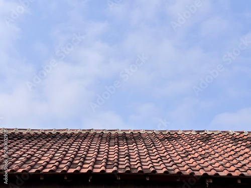 Minimalist old terracotta roof tiles against blue sky. Classic traditional house exterior background with large empty copy space.