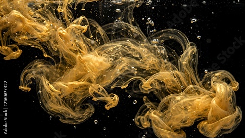 Abstract metallic gold ink swirling underwater with bubbles against black background
