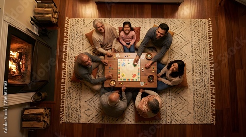 Happy multi-generational family playing a board game by the fireplace