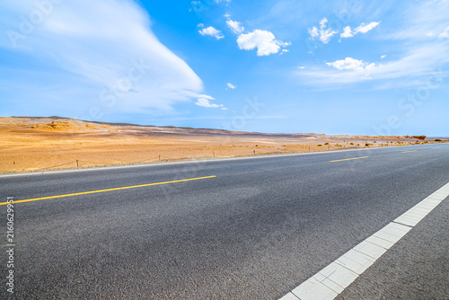 Fotografía Empty asphalt highway crossing the arid Dahaidao landscape in Xinjiang, China, with expansive desert terrain, vivid blue sky, and commercial travel appeal