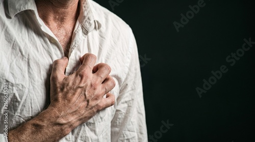 A man in a white shirt clutches his chest in pain, sweat visible on his skin. Medical emergency and acute cardiac distress. Men's Health 
