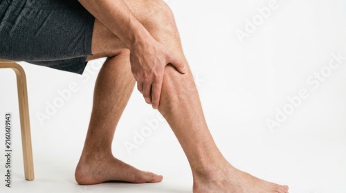 Man holding calf muscle in pain while sitting on stool