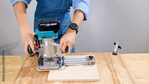 Fotografie Carpenter using a cordless electric wood router to shape a plywood board in a workshop