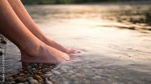 Bare feet wading in clear river water over smooth stones