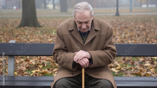 Sad elderly man sitting alone on park bench in autumn scenery