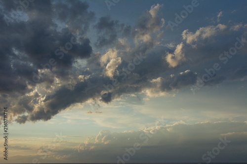 Fotografía Dramatic evening sky with dark clouds illuminated by soft golden light during sunset creating a serene and atmospheric landscape over a calm horizon