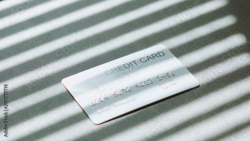 Financial privacy, silver credit card lying on surface with window blind light and shadow.