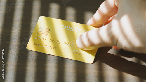 Financial privacy, Hand picking up Gold credit card under Venetian blinds light and shadow. Financial Debt Business concept.