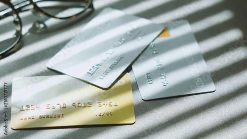Digital banking decisions, Multiple credit cards lying on office desk near glasses with window blind shadows.
