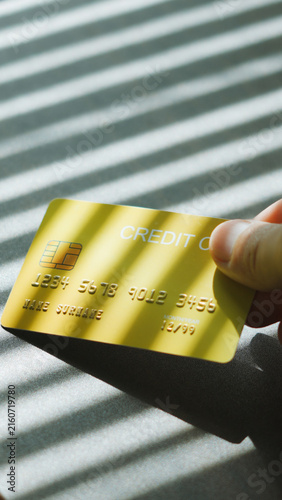 Personal banking, hand picking up gold credit card with warm sunlight and shadow effect. Cashless society concept.