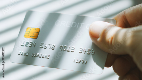 E-commerce spending, close up of hand reaching for silver credit card with Venetian blind lighting.