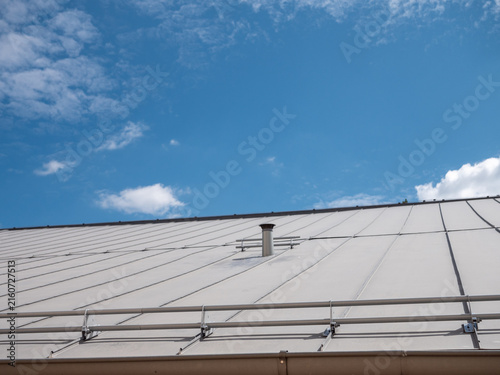 Foto Modern standing seam metal roof with snow guards and chimney under blue sky, showing rooftop safety equipment for snow retention, construction, roofing and building maintenance