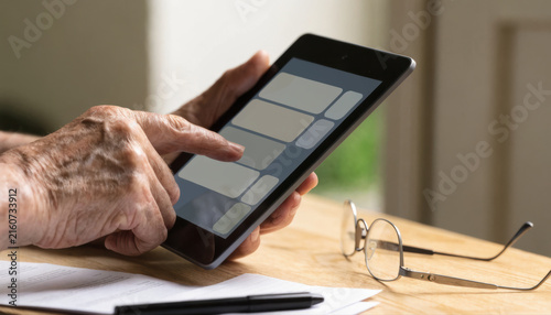 Elderly hand senior person tablet touch screen technology digital app interface indoors closeup aging communication modern lifestyle finger navigation glasses document pen table learning