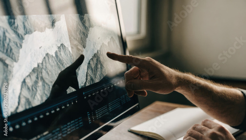 Hand finger computer monitor screen mountain landscape photo editing software Hand points computer monitor with mountain landscape photo editing software interface warm studio workspace environment