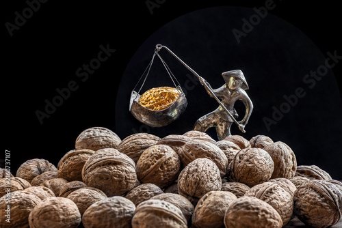 Silver figurine carrying golden walnut on balance scale with walnuts