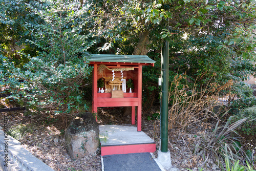 Foto Small red wooden Japanese Shinto miniature shrine (Hokora) surrounded by lush trees and green foliage in nature