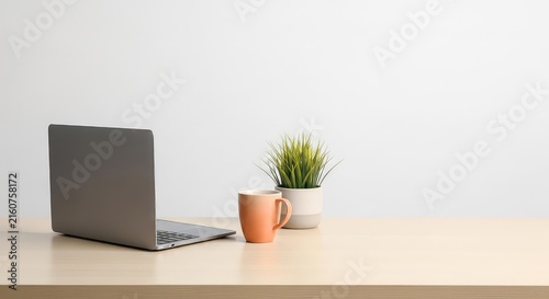 A clean and modern office desk features a sleek closed portable computer alongside a ceramic mug and a small green plant in a neutral pot, green, productivity, business