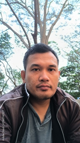 Portrait of Asian man wearing casual jacket outdoors in a park with tree background