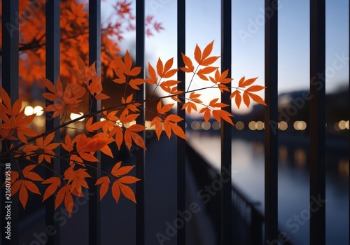 Autumn maple leaves with vibrant orange color glow behind a fence at dusk, with blurred city lights