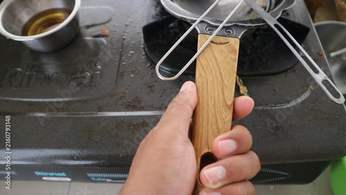 Fotografie Hand holding a pan handle on a dirty gas stove, preparing a meal in the kitchen