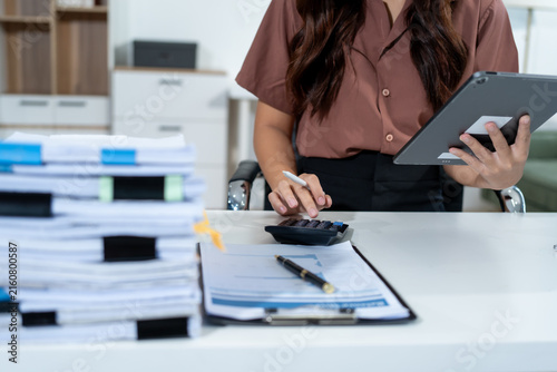 Canvas Print Businesswoman at office desk using a tablet and calculator beside stacks of paperwork, showing accounting, budgeting, finance, and busy administrative work