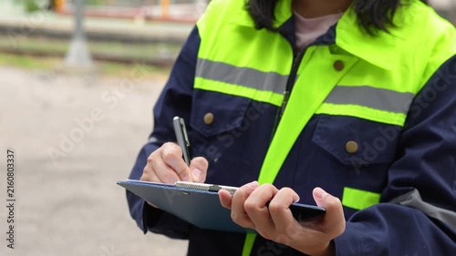 A safety officer is checking on hazardous chemical material checklist for risk assessment before tranportation the dangerous good with train tanker railway background. Industrail working scene.