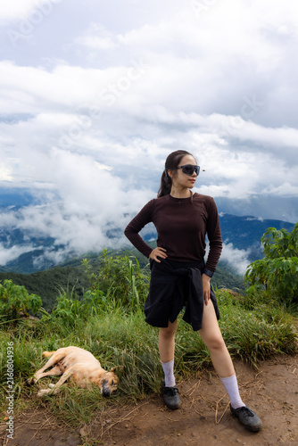 Foto Woman hiker standing on mountain trail with sleeping dog and dramatic cloudscape