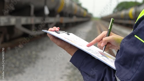 A safety officer is checking on hazardous chemical material checklist for risk assessment before tranportation the dangerous good with train tanker railway background. Industrail working scene.