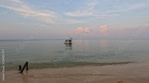 A single boat anchored near the shore on a calm beach at early morning on Phu Quoc island, Vietnam, showcasing a tranquil sea and serene tropical landscape.
