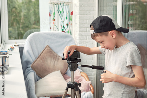 A boy adjusts a camera on a tripod while creating a stopmotion cartoon on a balcony. He arranges a small scene near the window, combining creative play, filmmaking and storytelling.