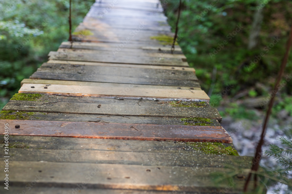 Fototapeta premium Wooden suspension footbridge close-up of weathered planks and rope walkway for outdoor banner or background design