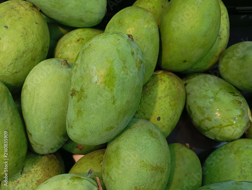 Canvas Print Fresh green raw mangoes piled together at a market for sale.