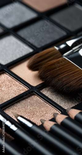 Close-up of an eyeshadow palette with brushes and pencils on a dark background