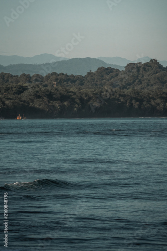 Calm rocky coastline with distant hazy mountains and a small orange boat on a tranquil sea, moody coastal seascape