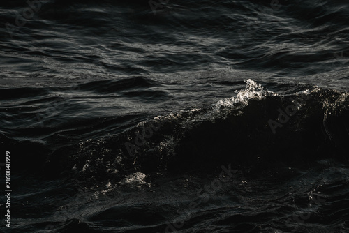 Moody close-up of dark ocean waves at night with a small illuminated crest and textured water surface