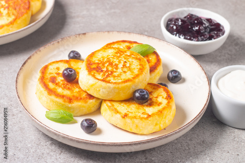 Golden cottage cheese pancakes with sour cream, blueberry jam and fresh berries. Healthy breakfast concept.