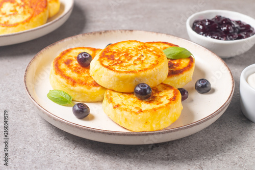 Golden cottage cheese pancakes with sour cream, blueberry jam and fresh berries. Healthy breakfast concept.