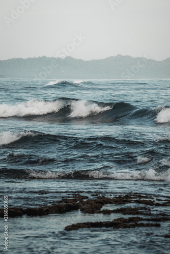 Photography Moody rocky shoreline with breaking ocean waves, foamy surf and distant headland